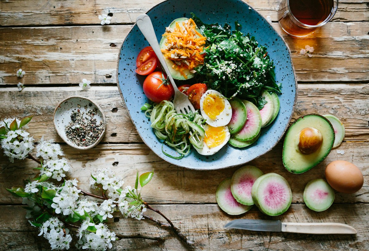 Teller mit Gemüse, Avocado, Ei und Salat auf einem Holztisch