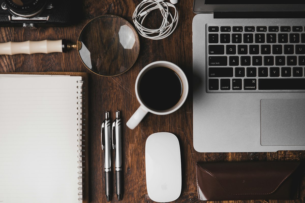 Schreibtisch mit Laptop, Kaffeetasse und Notizbuch von oben